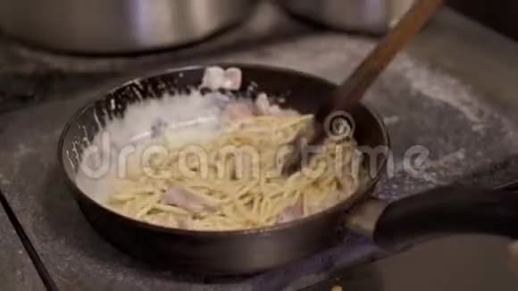 将搅拌好的意大利面条与芝士酱和切碎的培根放入热锅中煎煮视频的预览图