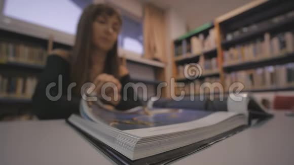 年轻的高加索女人在图书馆翻着插图书籍的一页离焦射击视频的预览图