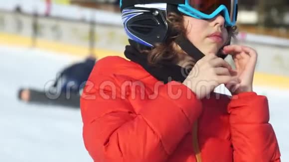 在滑雪场戴着头盔和护目镜的少年一个孩子用头盔系紧腰带滑雪安全肖像亲密视频的预览图