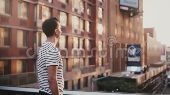 慢动作快乐的微笑年轻的西班牙裔男子站在惊人的日落纽约桥享受美妙的城市景色视频的预览图