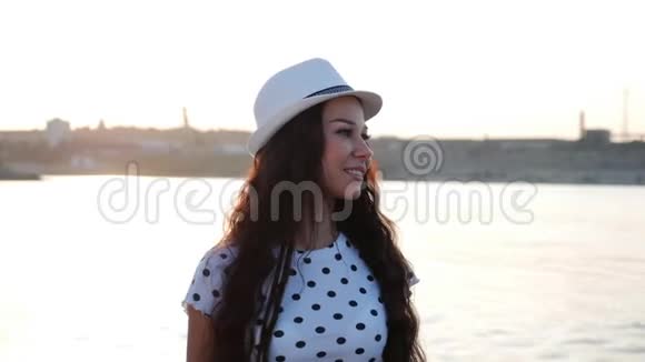美丽时尚快乐时尚年轻漂亮女孩戴着白色可爱的帽子走在海边沙滩上看着视频的预览图