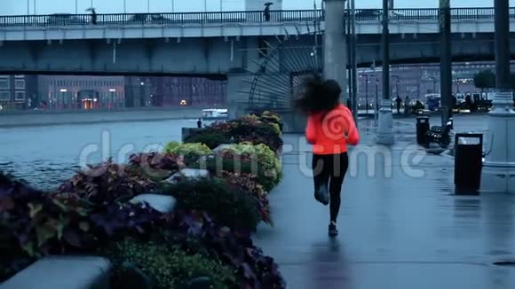 傍晚时分年轻的混血运动女运动员沿着城市公园的堤岸奔跑慢镜头视频的预览图