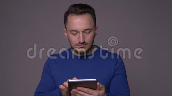 一位年轻英俊的白种人的特写镜头他在平板电脑上发短信看着背景与镜头隔绝视频的预览图