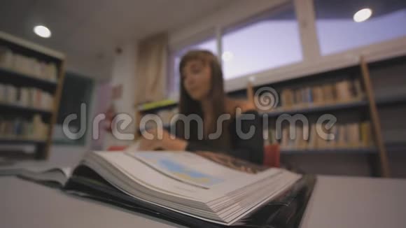 年轻的高加索女人在图书馆翻着插图书籍的一页离焦射击视频的预览图