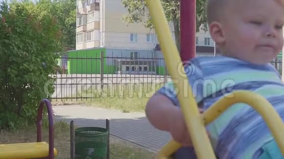 一个两岁的男孩在城市背景下骑着秋千的肖像慢动作视频的预览图
