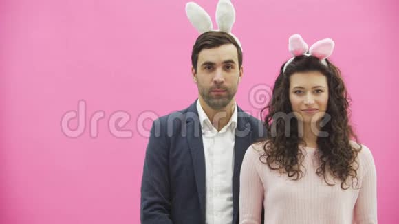 年轻漂亮的夫妇站在粉红色的背景上头上戴着黑黑的耳朵在这期间他和他妻子视频的预览图