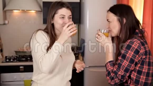 两个年轻女孩在厨房聊天边准备晚餐边喝橙汁视频的预览图
