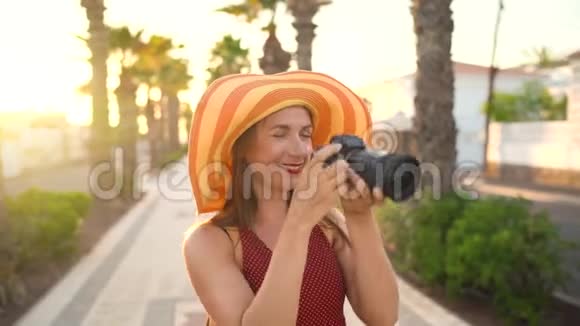 摄影女游客戴着一顶黄色的大帽子在夕阳下美丽的热带风景中用相机拍照视频的预览图