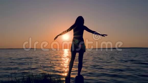 年轻女子的剪影在海上日落时举起双手侧着身子视频的预览图