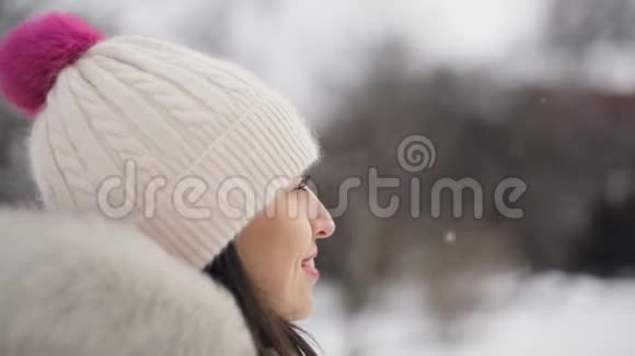 布鲁内特年轻的女人粉红色的嘴唇米色的羽绒衣和帽子象征着爱她的手是棕色的心视频的预览图
