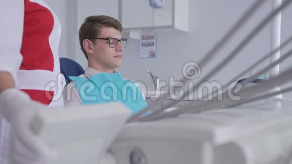 一位女牙医用带眼镜的年轻病人举起一把牙科椅视频的预览图