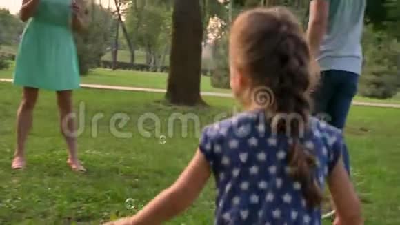 年轻的家庭夏天在公园散步女儿在捉泡泡童年的概念视频的预览图