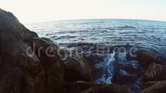 晚上岩石海岸和海浪拍打着阳光下的石头视频的预览图