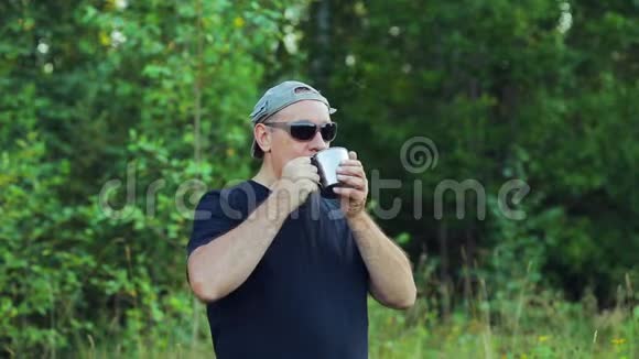 一个人站在森林的边缘喝着杯子里的茶欣赏着大自然视频的预览图