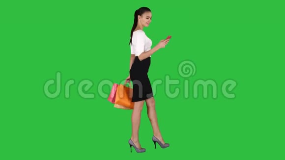 漂亮的年轻女人用手机走路拿着购物袋在绿色屏幕上Chroma键视频的预览图