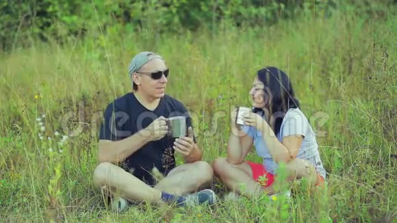 男女游客坐在草地上喝着杯子里的茶聊天视频的预览图