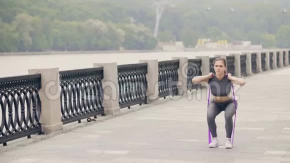 漂亮的女人与运动拓展者一起做蹲式锻炼视频的预览图