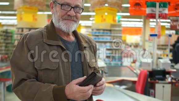 一个留着灰色胡子和眼镜的人正拿着一整个钱包在超市里微笑地看着相机关闭视频的预览图