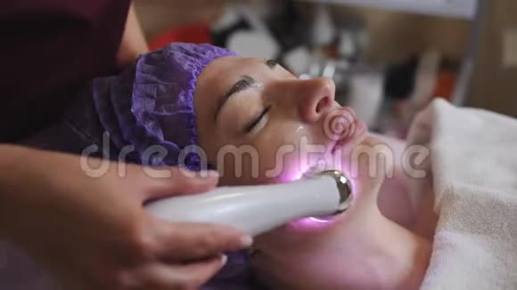 美容师带有微磨擦装置为躺在水疗中心的年轻妇女做面部去角质视频的预览图