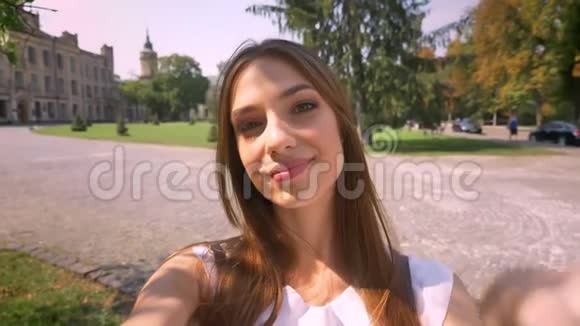 漂亮的年轻女人白天站在公园里拿着相机自拍展示和平标志交流理念视频的预览图