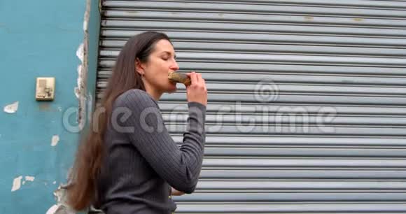 美丽的女人在城里散步时吃甜甜圈视频的预览图