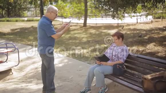 在公园里一位年迈的老人通过电话拍下了他年迈的妻子视频的预览图