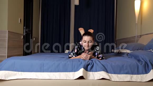 美丽的黑发女孩躺在床上用手机网上约会视频的预览图