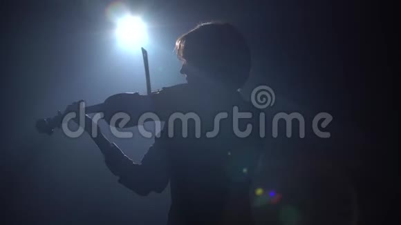 在一个黑暗的工作室里一个音乐家在那里拉小提琴黑烟背景背面视频的预览图