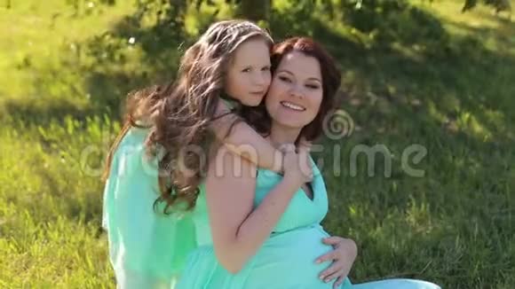 怀孕的母亲和一个穿着同样衣服的小女儿坐在草地上视频的预览图