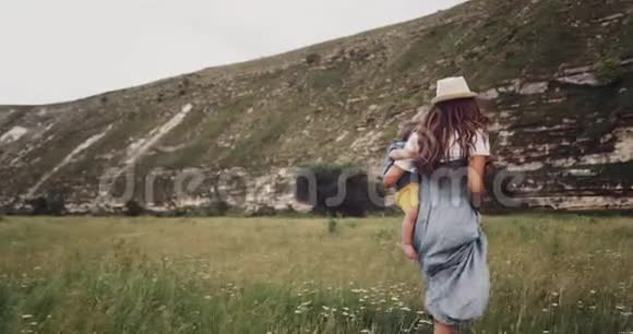 小女孩带着她的小男孩走过草地环顾四周在山的中间视频的预览图