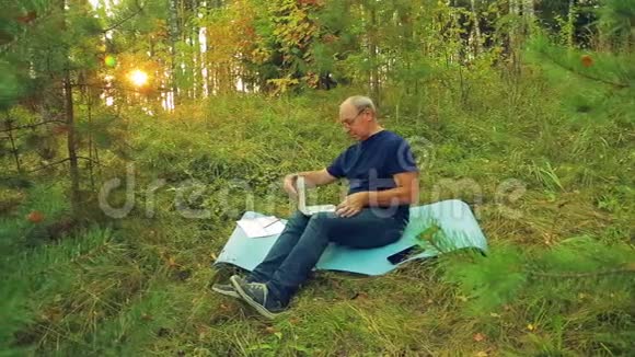 一个戴眼镜的人正在林间空地上用笔记本电脑键盘打字视频的预览图