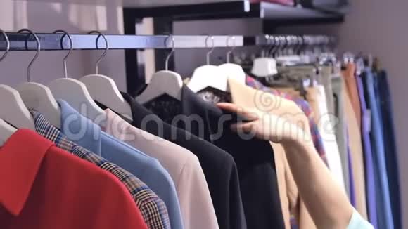 一个长头发的女孩通过挂在货架上的衣服在现代商店慢动作中寻找服装近景视频的预览图