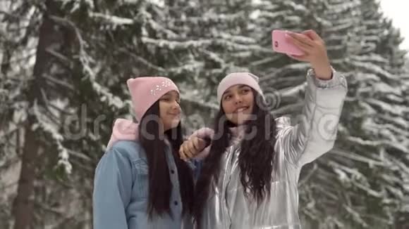 两个女朋友用智能手机在冬天森林的背景上自拍4K视频的预览图