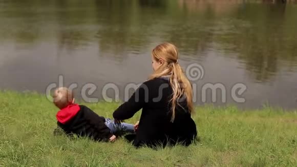一位快乐的母亲和她的儿子躺在春天河岸上的绿草上视频的预览图
