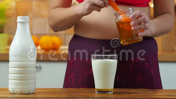 运动女孩把蜂蜜放进一杯杏仁牛奶里慢动作视频的预览图