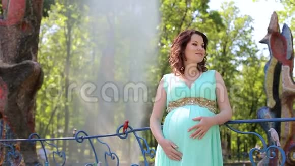 一个穿着长裙的怀孕女孩站在喷泉背景下的城市公园里视频的预览图