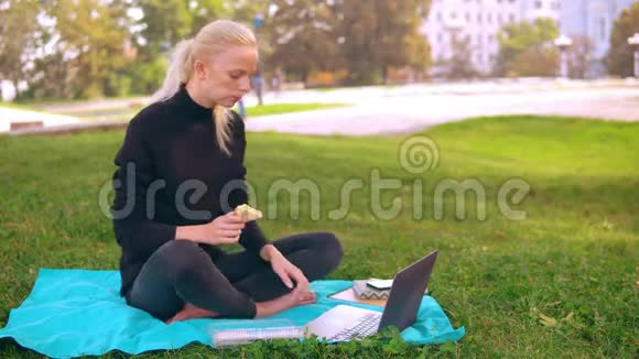 白种人女孩在户外的笔记本电脑上吃饭和打字视频的预览图