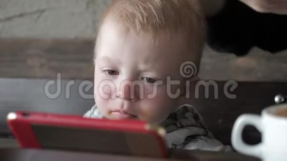 可爱的小男孩坐在咖啡馆里和父母通电话看动画片视频的预览图