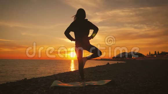 日落时分年轻美丽健康的女子在海边的莲花位置冥想的剪影年轻女子练习视频的预览图