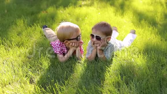 夏天两个快乐的小男孩戴着太阳镜躺在草地上视频的预览图
