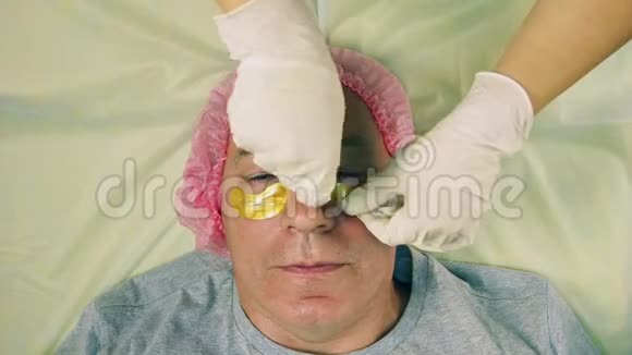 戴着手套的化妆师的女人的手在眼睛下面强加给男人的胶原蛋白垫视频的预览图