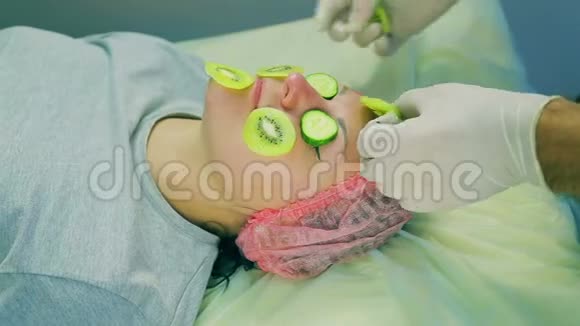 化妆师的男人的手从女人的脸上取出一个面具从猕猴桃片和黄瓜片中取出视频的预览图