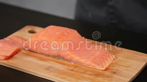 一位年轻的男寿司厨师用一把刀在桌子上切下一个熏鲑鱼锉刀双手戴手套特写视频的预览图