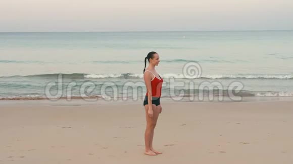 年轻健身女子马拉松运动员在日出前在热带海滩热身视频的预览图