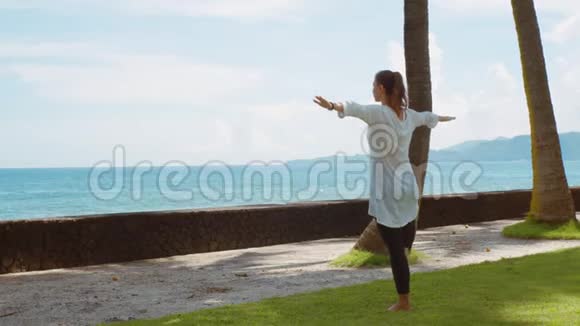 年轻的白种人女子在巴厘岛平静的海洋附近的海滩上练习瑜伽放松身心背景优美视频的预览图