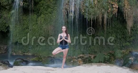 瀑布边的森林里冥想练习瑜伽的女人视频的预览图