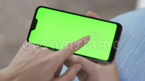 一个人使用带有触摸式绿色屏幕的手机浏览社交网络和交流特写视频的预览图