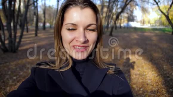 一个微笑的女人在秋天公园慢动作中盘旋的肖像4k60fps穿着外套的女孩走在秋天的城市里视频的预览图