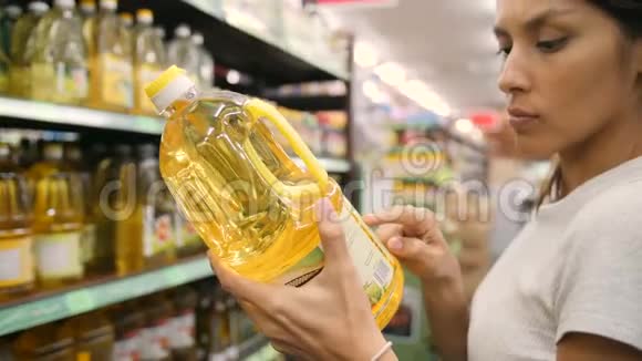 年轻的混血女人在超市里选择橄榄油顾客在商店里阅读配料标签4K视频的预览图