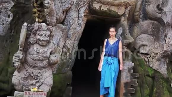 穿着蓝色衣服的可爱女人站在洞穴旁边有雕刻的脸型入口视频的预览图